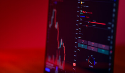 Bitcoin price is falling down and the entire crypto currency market is loosing money. The graph evolution of this coin on a laptop screen with red background. Strong sell signal.