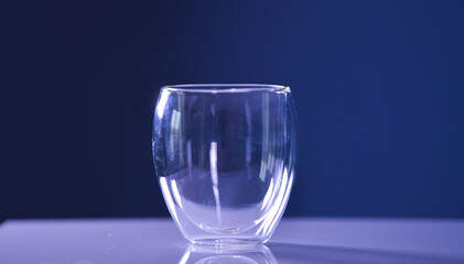 An empty transparent glass with double wall thermo resistant standing on a white table with dark background.
