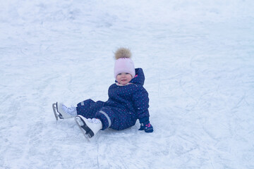 Fototapeta na wymiar Baby girl caucasian learns to skate at the ice rink in winter falls and laughs