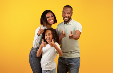 Hey, you. Excited black parents and their daughter pointing fingers at camera, standing over yellow...