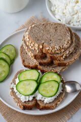 Slices of rye bread with cottage cheese and cucumbers on white background.