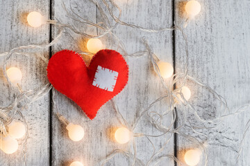 A wounded heart with a patch on a wooden background among a garland with lights. Valentine's Day