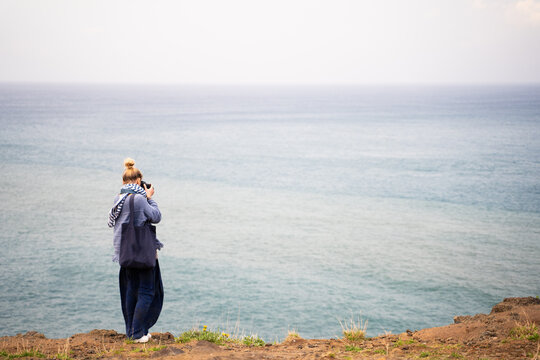 Woman standing taking photos of the sea from a cliff