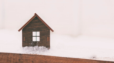 Obraz na płótnie Canvas Wooden toy house with windows and a roof in the snow drifts in the winter. Concept of the heating system and energy saving.