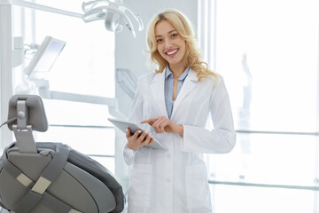 Attractive female dentist with digital tablet smiling at camera