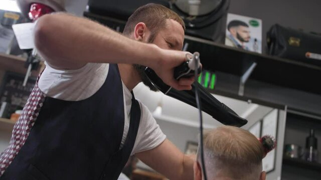 barbershop, professional male hair doer styling with a hairdryer and a comb to a stylish elderly man in the salon