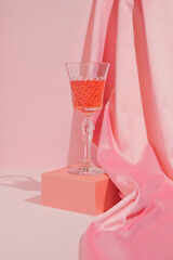 Pastel pink Valentine's Day or birthday composition with wine glass and satin on pastel background....