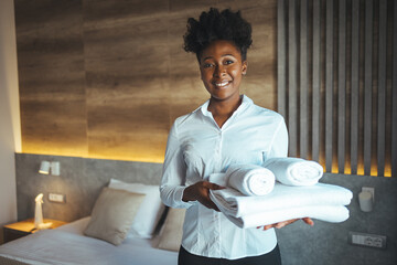 Maid putting stack of fresh white bath towels on the bed sheet. Room service maid cleaning hotel room. Maid making bed in hotel room. Change of towels in the hotel room - obrazy, fototapety, plakaty