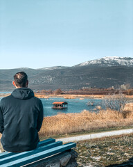 a man is staring at the View of Vegoritida lake in Pella Greece in the background the mount Voras with a bit of snow on a bright day