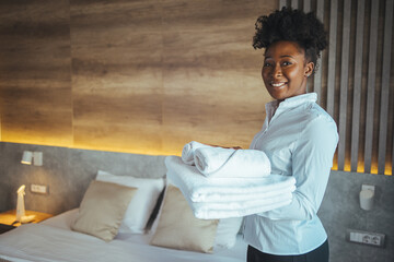 Woman with curly hair and dressed in maid uniform of a luxurious hotel arranges the towels of...