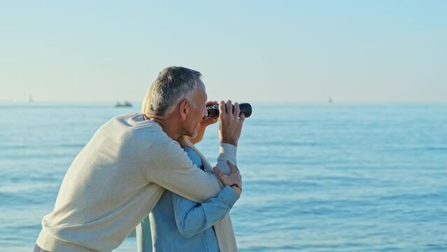 Couple standing at the sea looking through binoculars