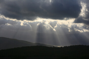Naklejka na ściany i meble Beams of light from behind the clouds in the valley above the hills