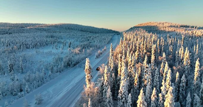 Aerial drone view following a car driving in middle of snowy trees in Lapland - circling, drone shot
