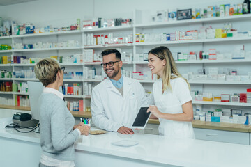 Two pharmacist giving prescription medications to senior female customer in a pharmacy