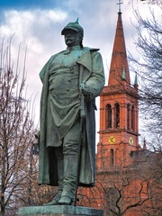 Denkmal des Kanzlers des Deutschen Reichs Otto von Bismarck in Höchst am Main mit der evangelischen Stadtkirche im Winter, umgeben von kahlen Bäumen und bei wolkigem Wetter