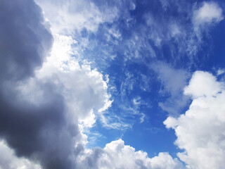 Lush clouds overhead in the sky block the sunlight. Through the layers of clouds, a blue sky peeks through. It's raining soon. Horizontal photo.