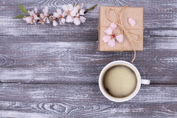 Spring composition with coffee, a gift wrapped in craft paper, spring blossoming almond branches with flowers on a gray shabby wooden table. Flat lay, copy space