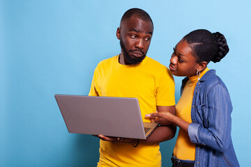 Modern people looking at computer screen over blue background, browsing internet and social media application for fun. Boyfriend and girlfriend using laptop with technology in studio.
