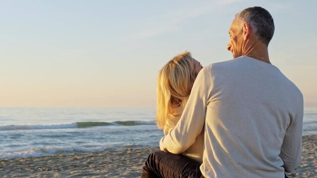 Mature couple sitting on the beach looking at sea