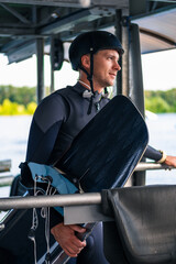 Confident smiling wakeboarder in full gear with board staning on start dock