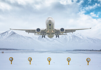White passenger aircraft take off from winter airport runway against the backdrop of scenic snow-capped mountains