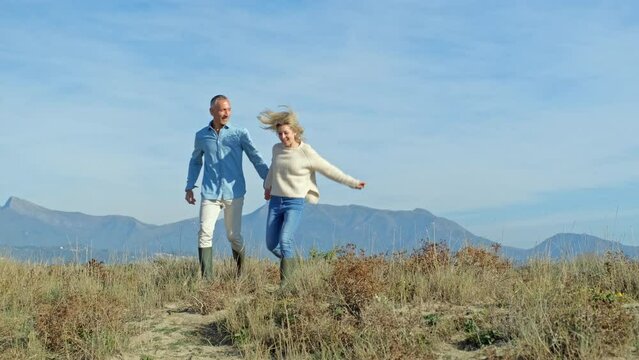 Happy mature couple running in nature holding hands