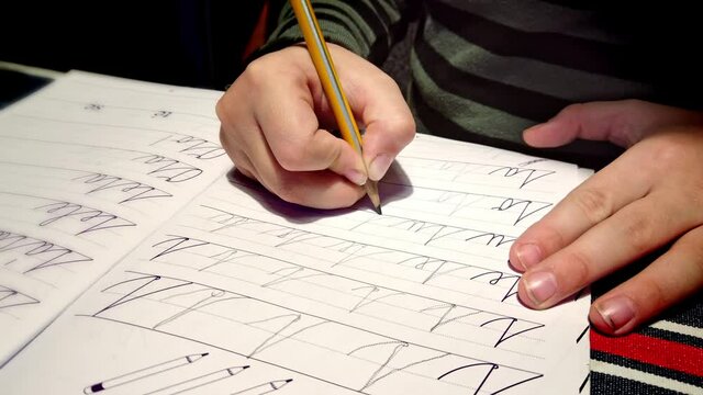 Child sitting at table practicing joined up writing homework repetition in lined notebook close up