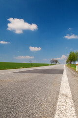 Asphalt road through the green field and clouds on blue sky the spring
