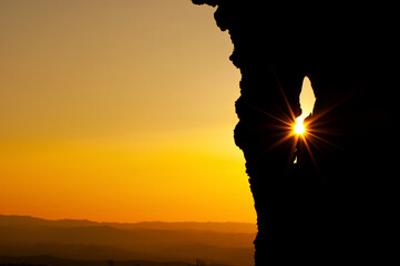 Tree silhouette and sunrays protruding through hole in the tree at sunset