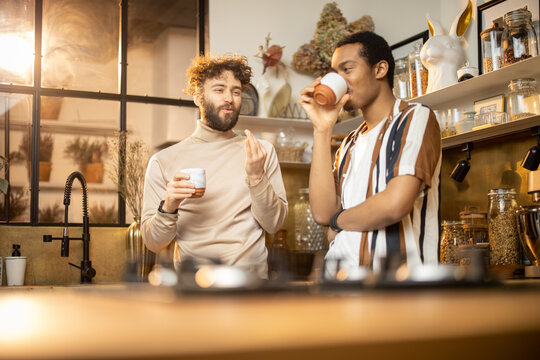 Two guys of different ethnicity having warm conversation while drinking coffee on kitchen at home. Concept of close male friendship or relationship as gay couple. Caucasian and hispanic man together