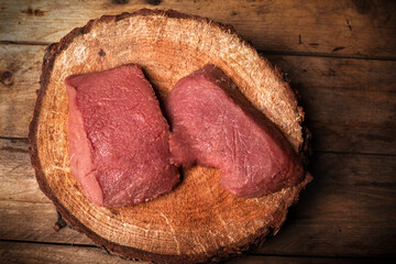 Top view of raw game meat, beef. Steaks, pieces of red meat on chopping block, wood slice. High...