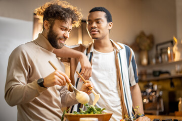 Fototapeta na wymiar Two guys of different ethnicity having fun while making salad together on kitchen. Concept of gay couples and everyday life at home . Caucasian and hispanic man cooking healthy food