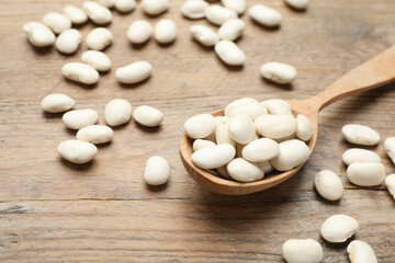 Fototapeta na wymiar Raw white beans with spoon on wooden table, closeup
