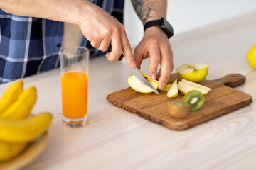 Unrecognizable mature man cutting fruits for smoothie or fresh juice, preparing meal at kitchen table