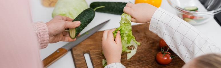 top view of cropped woman and child near fresh vegetables on kitchen table, banner.