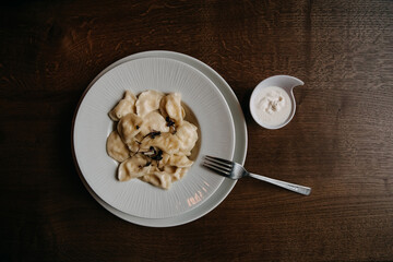 Traditional homemade cottage cheese dumplings with sour cream served on a white plate, top view.