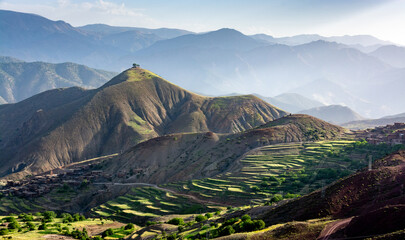 The Atlas Mountains in Morocco. Two solitary trees on top of a mountain overlook a village and terraced cultivated fields