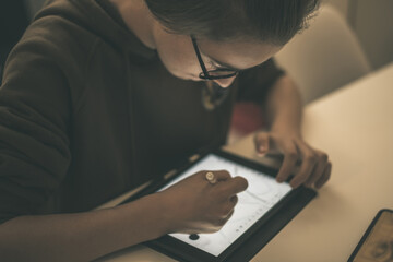Fototapeta premium Teenager drawing with tablet and virtual pen. Millennial student doing homework with new technology devices. Young boy draw on pad at home. Male hands working with digital pencil on the touch screen.