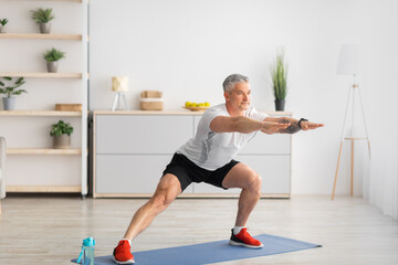 Home workout. Active mature man doing side lunges, stretching legs on yoga mat in living room, copy...