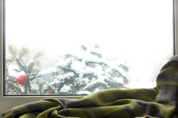 green plaid against the background of snow-covered spruce branches outside the window. cozy winter day at home