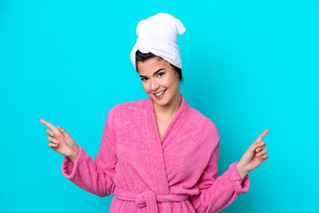 Young Brazilian woman with a bathrobe isolated on blue background pointing finger to the laterals and happy