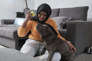 Young muslim woman playing with her grey sharpei dog at home.