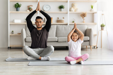 Sporty father and daughter sitting on fitness mat, meditating