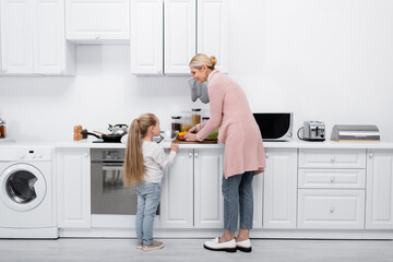 smiling mature woman with little granddaughter cooking together in modern kitchen.