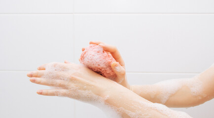 A girl in a white bathroom in foam rubs her hands with a pink washcloth