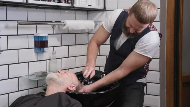 barbershop, professional male master stylist washes the hair of an older man for a haircut and styling in a hairdresser