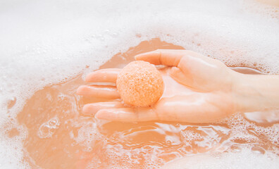 A girl in a white bathroom with foam dissolves a bright bath bomb in water