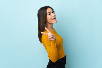 Teenager girl isolated on blue background smiling and showing victory sign