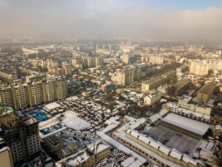 Fototapeta premium Aerial black and white winter top view of modern city center with tall buildings and parked cars on snowy streets.