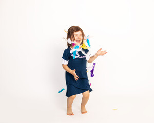 Laughing preschool barefooted fair-haired girl playing with colourful feathers and jumping over white studio background